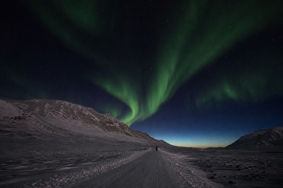 Green aurora over a snow-covered valley outside Longyearbyen during the middle of a polar night day